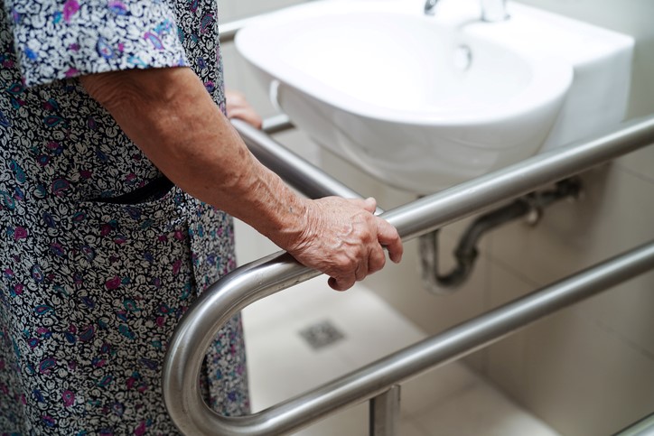 An elderly person holding bathroom grab bars near the sink in Houston, TX